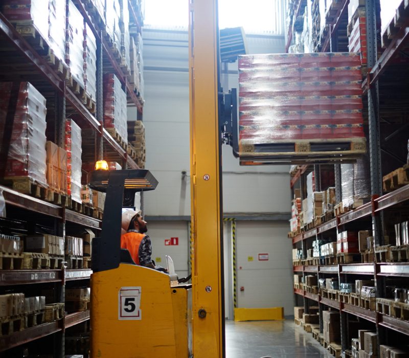Loader lifting packed goods on shelf of storehouse