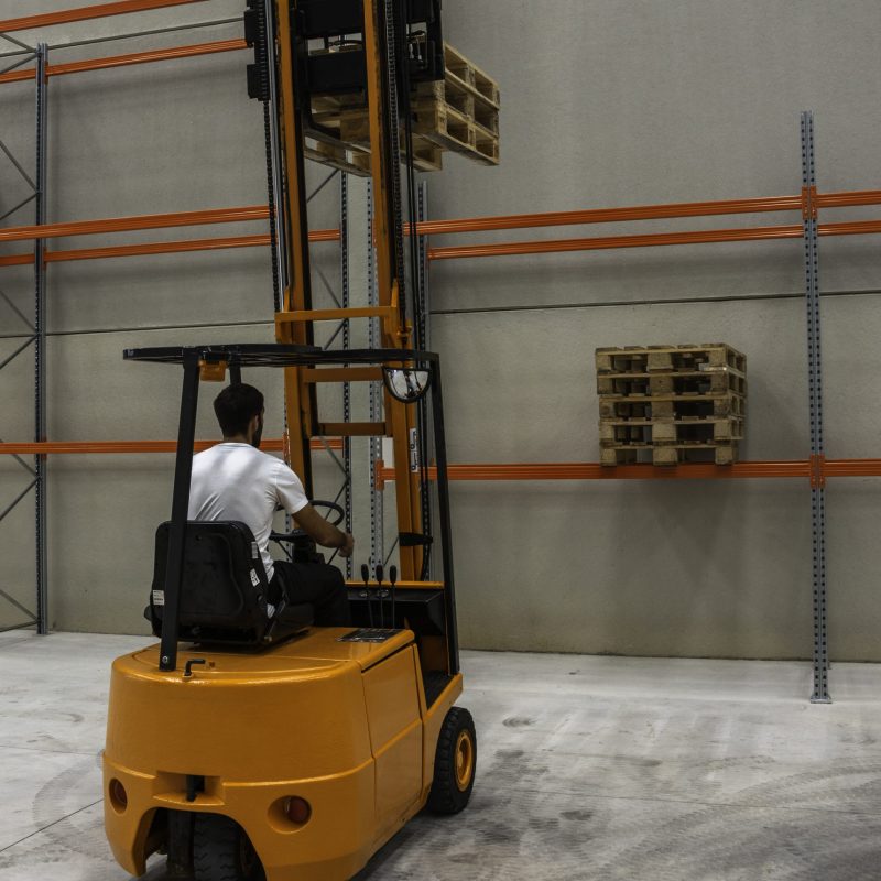 A vertical shot of a male operating an industrial lifting machine in a warehouse